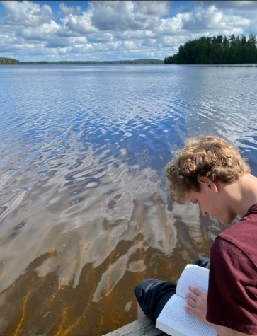 Thomas Short reads beside the water in the pristine Finland environment.