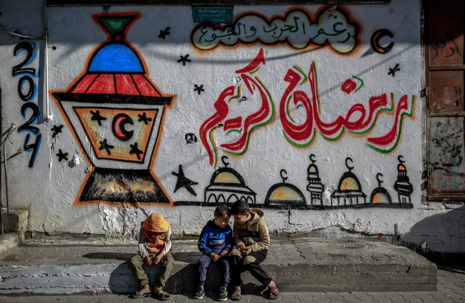 Palestinian children sitting in front of Ramadan mural on March 8, 2024.