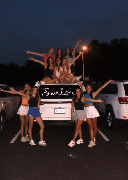 Taylor Clingenpeel, Morgan Turcotte, Reagan Nestlerode, Kendall Hart, Lily Sanborn, and  Lena Smith are on top of car while Delaney Ballum, Hadley Nowlan, Olivia Wetzel, and Christina Parlentari stand to the side.